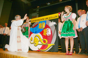 Die Ehrendamen Seraina Räss und Melanie Burkhalter halten die Vereinsfahne, während Pfarrer Marcel Ruepp sie segnet.
